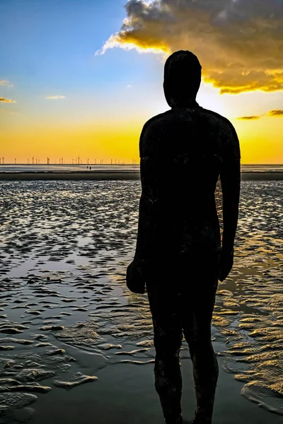 Crosby Beach, İngiltere 'de bulutlu bir günbatımında başka bir yerde bir heykelin dikey çekimi