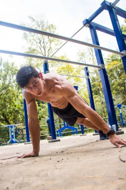 Parkta egzersiz yapan genç, üstsüz bir sporcu.