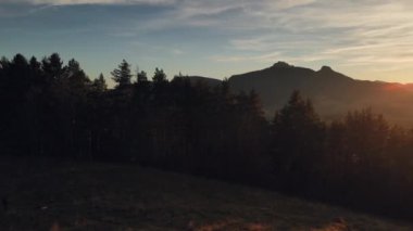 Ufukta güneş parlayan bir orman ve dağların panoramik görüntüsü.