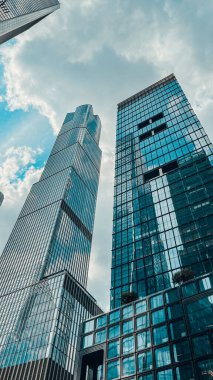 Mavi bulutlu gökyüzüne karşı camdan pencereleri olan modern bir gökdelenin alçak açılı bir görüntüsü.