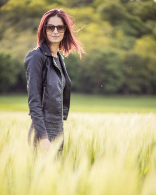 Güneşli bir günde tarlada uzun yeşil çimlerin arasında duran beyaz bir kadının güzel bir portresi.