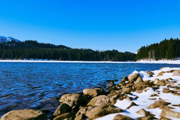背後には雪に覆われた岩場の海岸近くの湖の景色と雲一つない空 — ストック写真