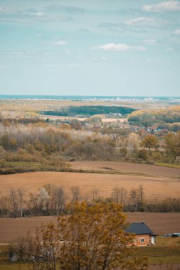 Kırsal kesimde bulutlu bir gökyüzünün altında yeşilliklerle çevrili bir kasabanın dikey görüntüsü.