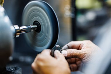 Bir erkek eli fabrikadaki bir makineye yüzüğün taşını oyuyor.