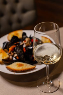 Bir tabak beyaz şarapla bir tabak midyenin dikey çekimi.