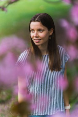 Etrafı kiraz çiçekleriyle çevrili gülümseyen bir kadın.