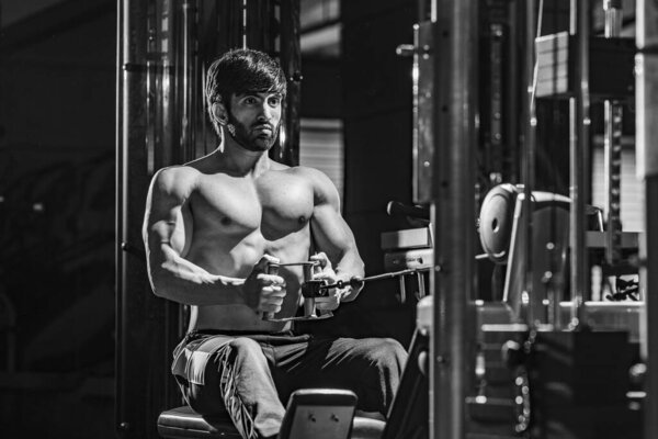 A grayscale shot of a fit athletic muscular Caucasian man working out at the gym