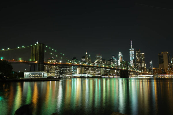 The Brooklyn Bridge and the New York City skyline with the reflections of lights in the bay at night