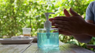 Masanın yanında ellerini dezenfektanla temizleyen bir adamın seçici odak noktası.