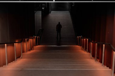 Merdivenler arasındaki yeraltı tünelinde tek başına duran bir adamın silüeti.