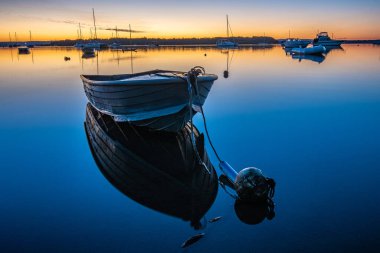 Renkli bir günbatımı arka planında kıyıya yakın bir teknenin resimli görüntüsü.