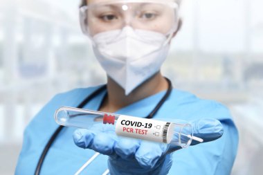 Bir NHS teknisyeni elinde COVID-19 bez toplama seti beyaz PPE koruyucu elbise ve maske takıyor.