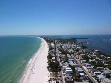 Açık mavi gökyüzünün altında beyaz bir kumsal ve sahil manzarası.
