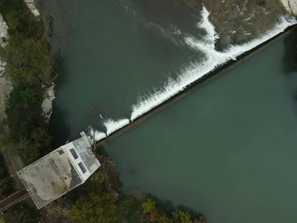 緑と建物に覆われた堤防を流れる川の上のダムの空中展望 — ストック写真