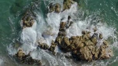 Drone tropikal bir okyanusun üzerinde uçuyor ve dalgalar kayalıklara çarpıyor.