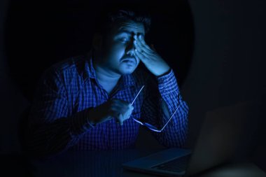 Genç adam gece yarısı dizüstü bilgisayar kullandıktan sonra gözlerini dinlendiriyor.