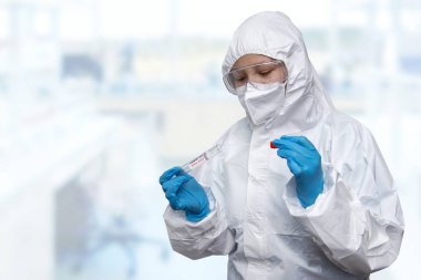 Bir NHS teknisyeni elinde COVID-19 bez toplama seti beyaz PPE koruyucu elbise ve maske takıyor.