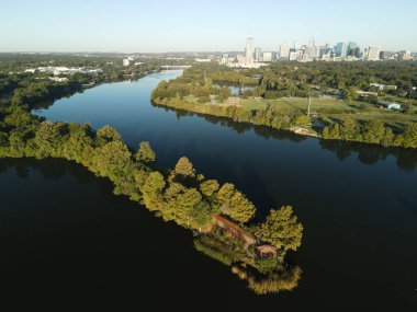 Bir nehrin kuş bakışı manzarası kıyılarındaki yeşil ağaçları mavi gökyüzünün altındaki şehir merkezine yansıtıyor.