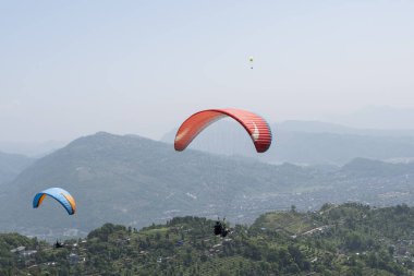 Pokhara dağlarında güzel bir bahar günü, Nepal 'de yamaç paraşütçüleri sisli gökyüzünde uçuyor.