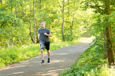 Güneşli bir günde parkın girişinde koşan beyaz bir adamın güzel bir portresi.