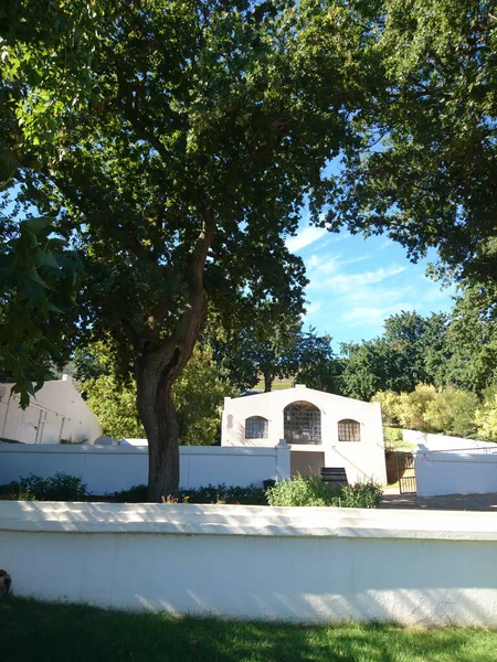 A vertical shot of an old white building surrounded with green trees in Suid-Agter-Paarl
