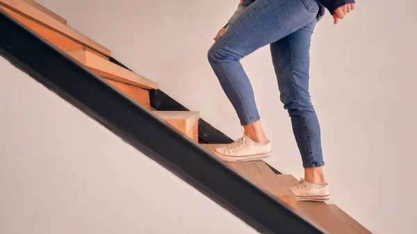 Legs of a Caucasian young woman wearing jeans and white sneakers and going upstairs