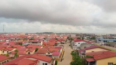 Bulutlu gökyüzünün altında kırmızı çatıları olan benzer evleri olan bir şehir manzarasının hava görüntüsü.