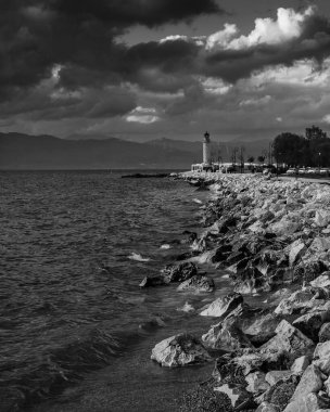 Kara beyaz bulutlu bir günde kayalık bir sahil ve deniz fenerinin dikey görüntüsü.