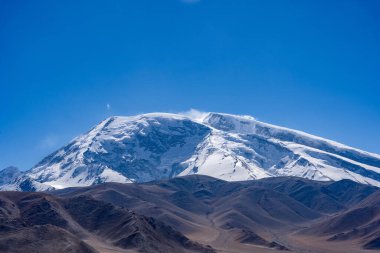 Güneşli bir günde kar kaplı dağların arka planında güzel bir tepe görüntüsü.