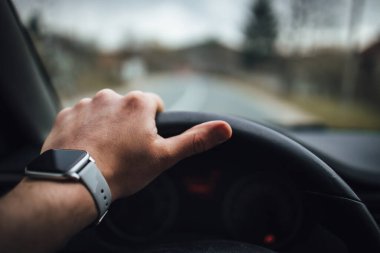Bir insan eli direksiyonu tutuyor ve akıllı saat takıyor..