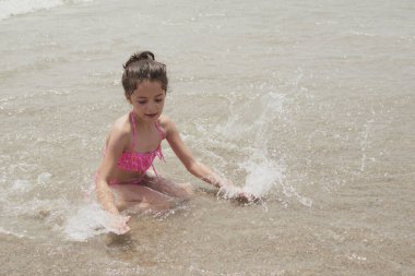 Pembe bikinili kız güneşli bir yaz gününde kumsalda dalgalarla mutlu mesut oynuyor, Vera, İspanya