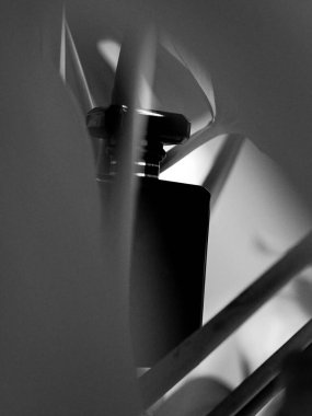 Canavar yaprakları arasındaki siyah parfüm şişesinin bulanık arkaplanlı gri tonlu derinlik görüntüsü.