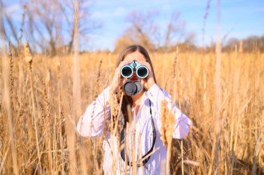 Gün boyunca bataklıkta kedi kuyruğu tarlasında duran mavi dürbünle kameraya bakan bir kadının üzerine..