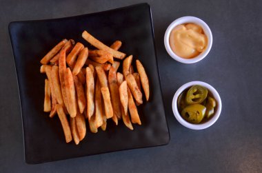 Patates kızartmasının siyah bir tabakta soslu ve jalapeno biberli hali.