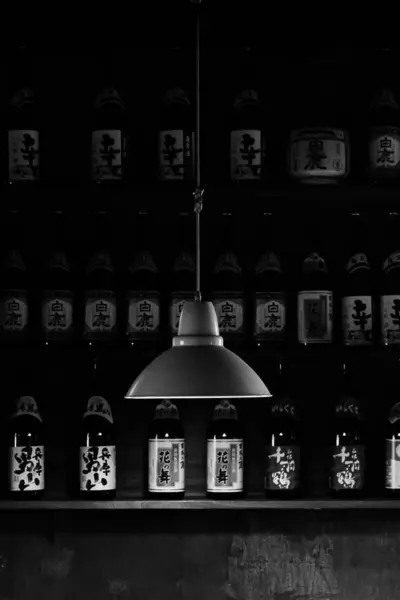 Вертикальный Драматический Снимок Висящей Черной Лампы Фоне Бутылок Азиатскими Символами — стоковое фото