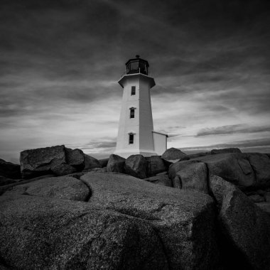 Büyük desenli gri pullu kayalarla çevrili beyaz bir deniz fenerinin alçak açılı görüntüsü.