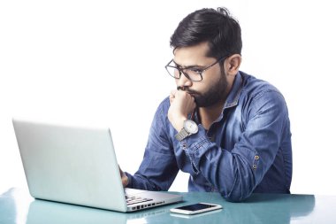 Genç yakışıklı beyaz arka plandaki dizüstü bilgisayara bakarak düşünüyor ve planlıyor.