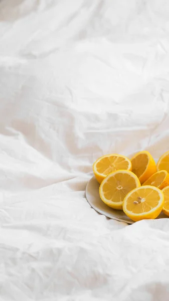コピースペースの白いベッドシート上のプレート上の半カットのレモンの垂直ショット — ストック写真
