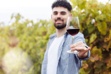Üzüm bağında bir kadeh şarapla genç, mutlu bir beyaz şarap garsonu.