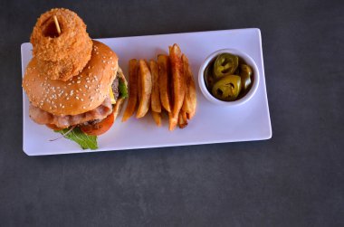 Hamburger, patates kızartması ve beyaz bir tabakta servis edilen Jalapeno biberi dilimlerinin üst görüntüsü.