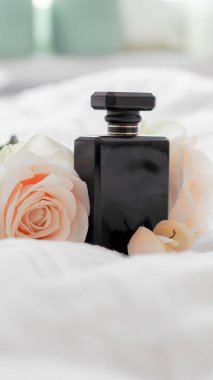 Siyah parfüm şişesinin yakın plan resmi. Çiçekli beyaz bir çarşaf üzerinde.