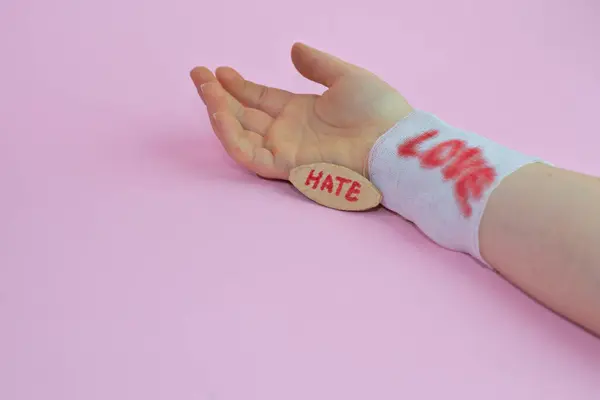 手首に Love と書かれた白いガーゼの男の手と Hate と書かれた木の板 — ストック写真