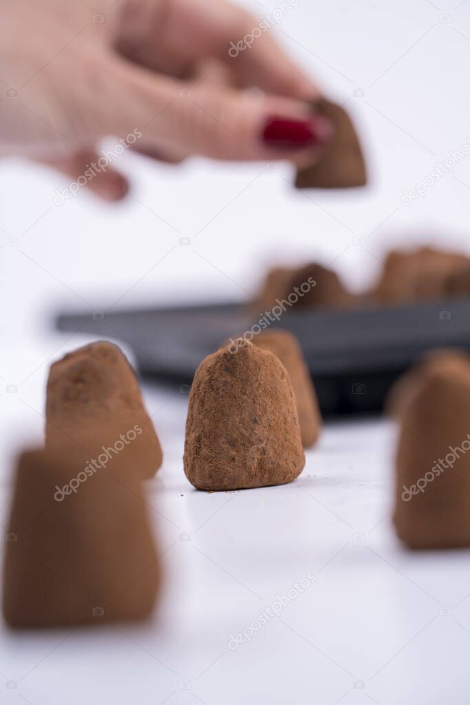 A vertical selective focus shot of a woman's hand lining up truffles on a shite table