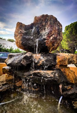 Devasa bir kayadan kayalık bir çeşmeye akan ince bir suyun dikey görüntüsü..