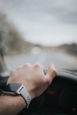 Direksiyonu tutan ve akıllı saat takan bir insan elinin dikey görüntüsü..
