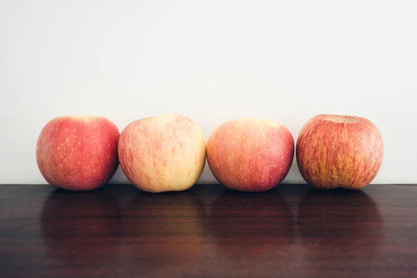 A closeup shot of four apples on the table on the background of a white wall