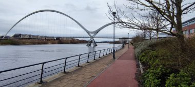 Nehir kıyısında binalarla kaplı modern bir köprünün manzarası.