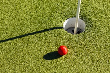 Gol deliğine yakın kırmızı bir golf topunun üst görüntüsü.