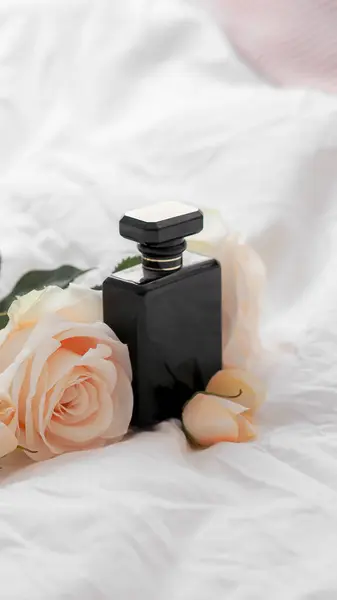 美しい花と白いシートの上に黒香水のボトルのクローズアップショット — ストック写真