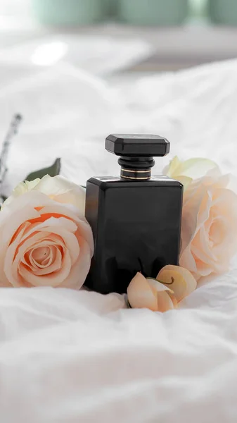 美しい花と白いシートの上に黒香水のボトルのクローズアップショット — ストック写真
